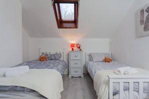 A bedroom with two beds, a nightstand with a lamp, and a window with a view of trees.