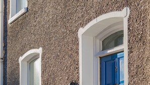A building with a textured facade, a blue door, and a small window with a white frame. - Windsor House - A Home from home (Derry)