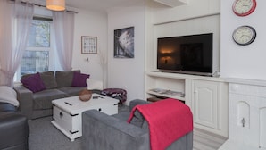 A modern living room with a grey sofa, a white cabinet, a flat-screen TV, and a fireplace. - Windsor House - A Home from home (Derry)