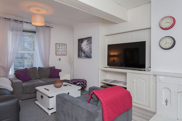 A modern living room with a grey sofa, a white cabinet, a flat-screen TV, and a fireplace.
