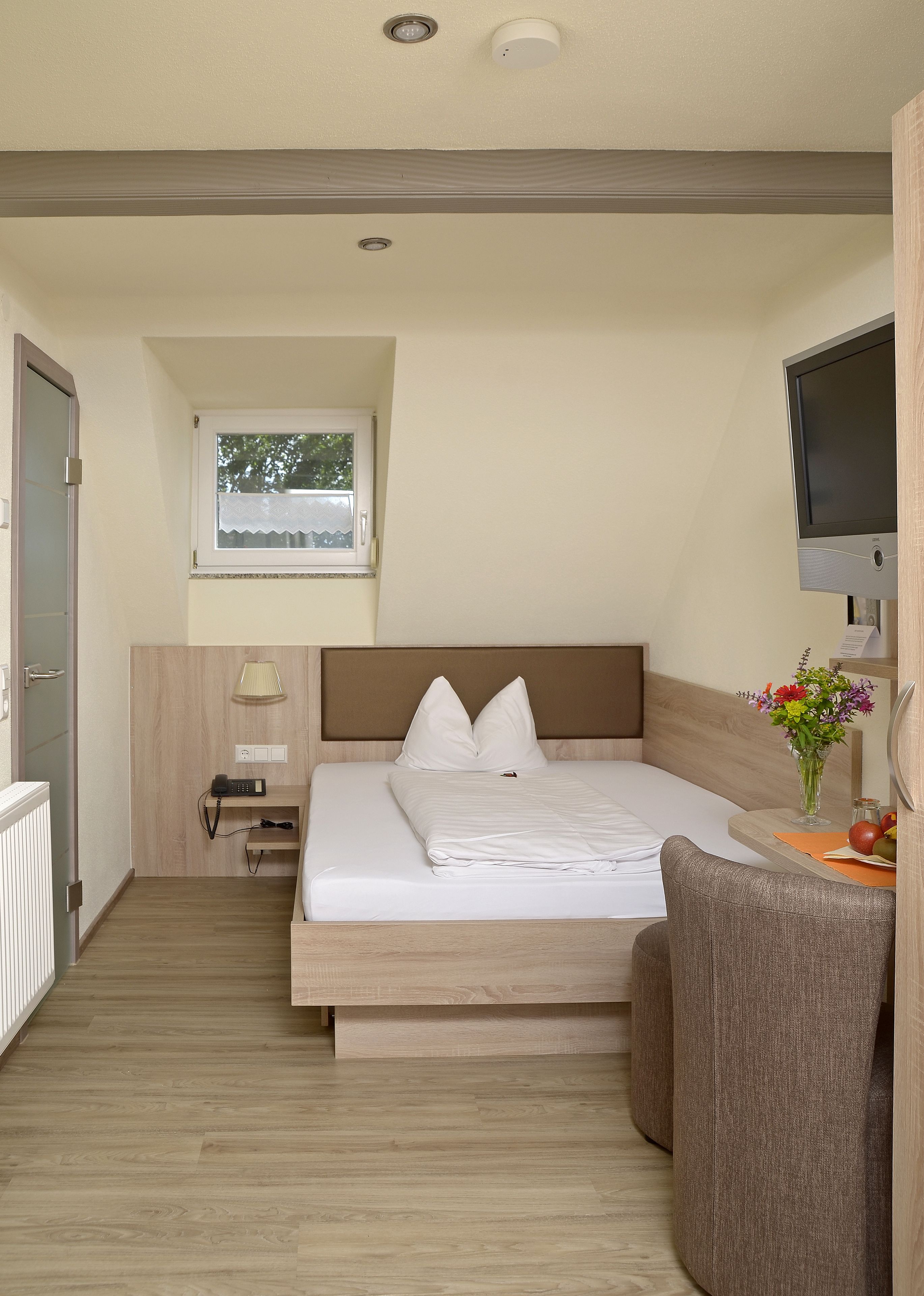 A bedroom with a bed, bedside table, lamp, and a TV on a stand.