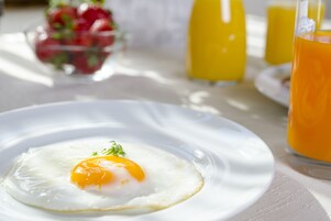 A breakfast plate with a sunny-side-up egg, a glass of orange juice, and a bowl of fruit in the background.