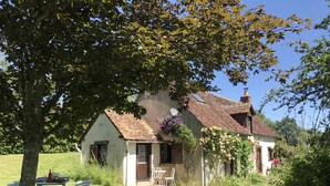 A traditional house with a tiled roof, a garden with a table and chairs, and a tree in the foreground. - Private detached stone house overlooking a lake (Sazeray)