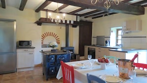 A kitchen with a dining area, featuring a stove, microwave, and a large wooden beam ceiling. - Private detached stone house overlooking a lake (Sazeray)