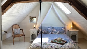 A cozy attic bedroom with a sloped ceiling, a floral bedspread, a wooden chair, and two bedside tables with lamps. - Private detached stone house overlooking a lake (Sazeray)