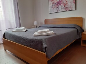 Una cama bien hecha con una colcha gris y dos toallas blancas dobladas a un lado.