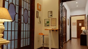 Pasillo de hotel con una puerta de madera, un escritorio con teléfono y un taburete de bar.
