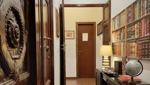 Un pasillo con puertas de madera, un escritorio con lámpara y un globo terráqueo, y una estantería llena de libros.