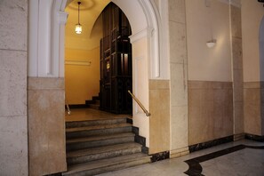 Eine imposante Treppe mit Marmorstufen und einem Geländer, die zu einem Raum mit hoher Decke und einem Kronleuchter führt.