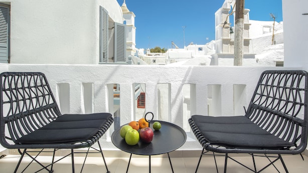 Een balkon met twee zwarte wicker stoelen en een klein rond tafeltje met fruit erop.