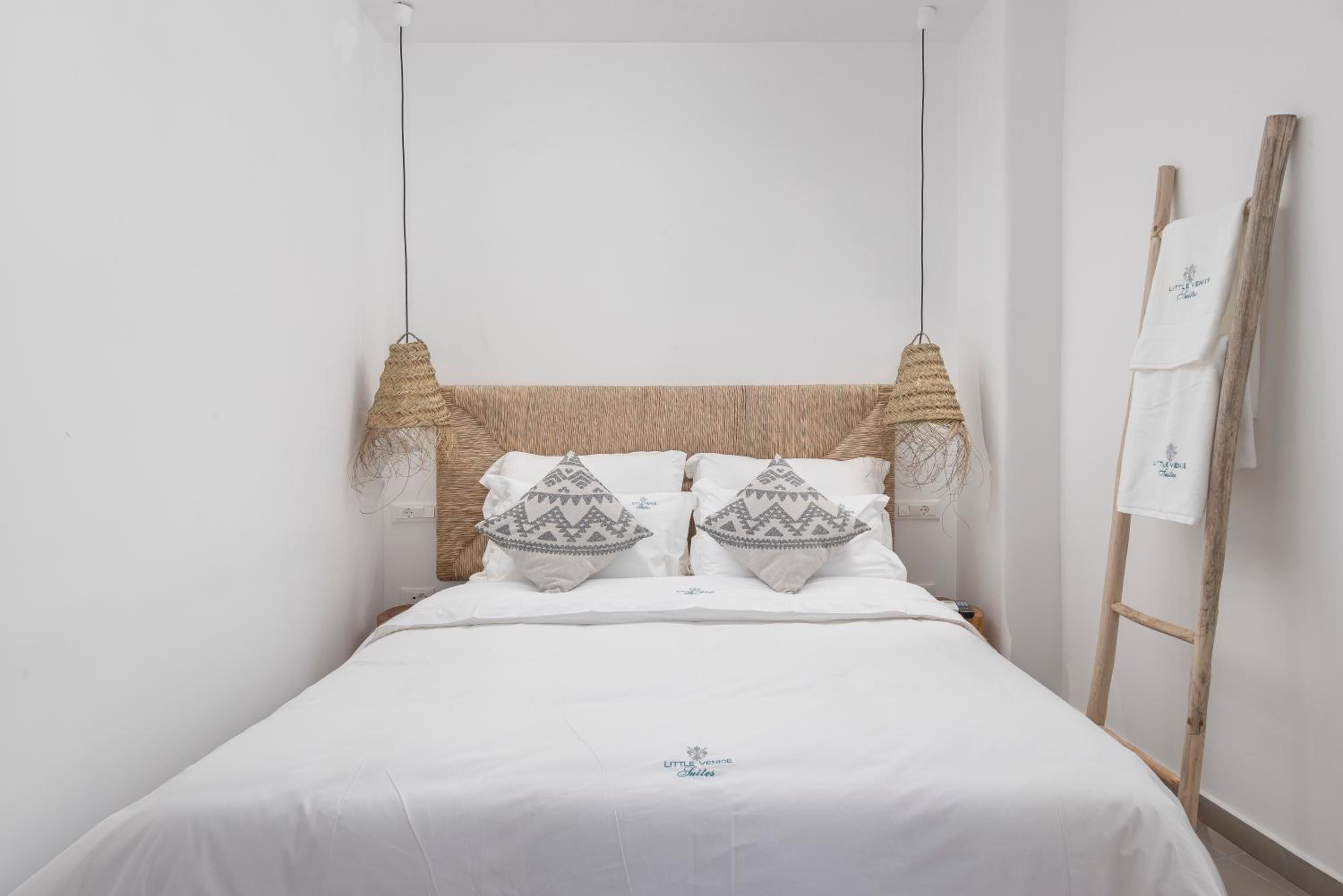 Een netjes opgemaakt bed met witte lakens, twee decoratieve kussens en een geweven hoofdbord.