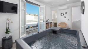 Een moderne badkamer met een bad, douche en toilet. Er is een televisie aan de wand en een potplant op de vloer.
