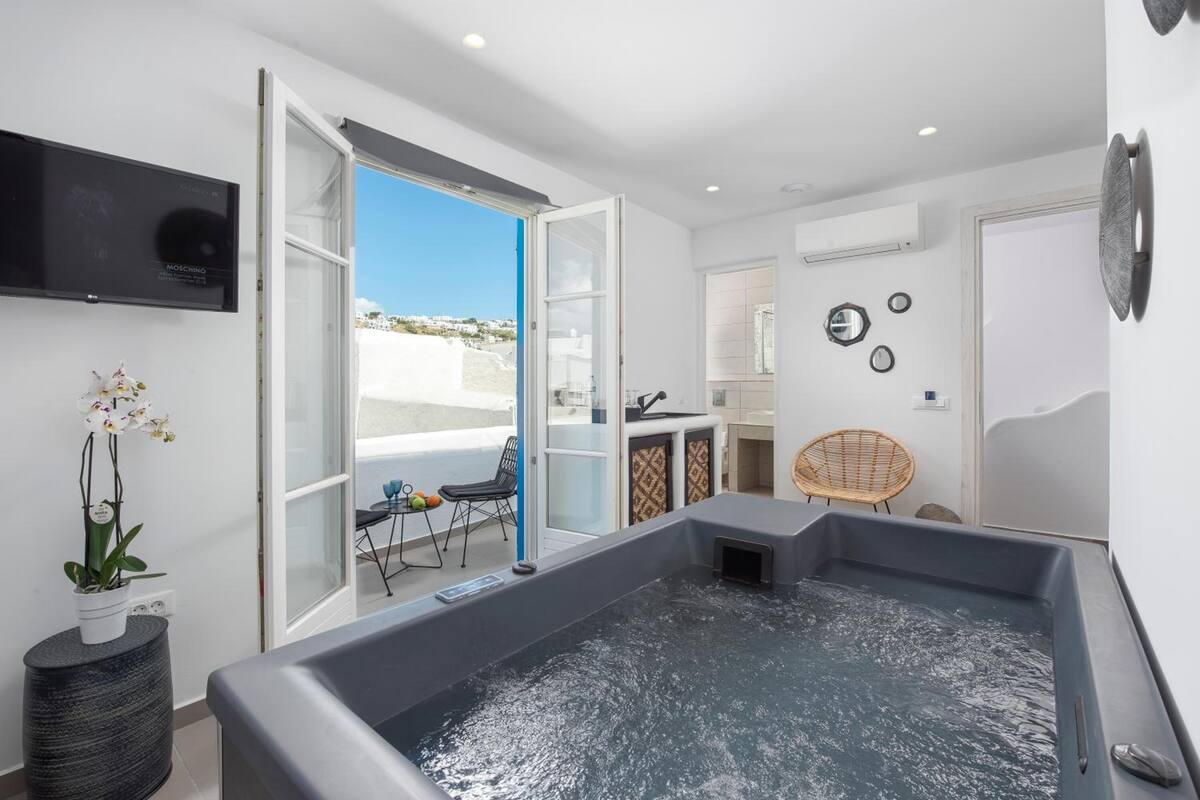 Une salle de bain moderne avec une baignoire, un espace douche et des toilettes. Un téléviseur est fixé au mur et une plante en pot est posée sur le sol.