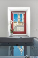 A bathroom with a red door, a potted orchid, and a bathtub with a clear view of the outside.