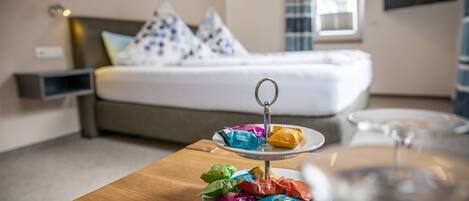 Una habitación de hotel con cama, una mesita de noche con una bandeja de bocadillos coloridos y un vaso de agua.