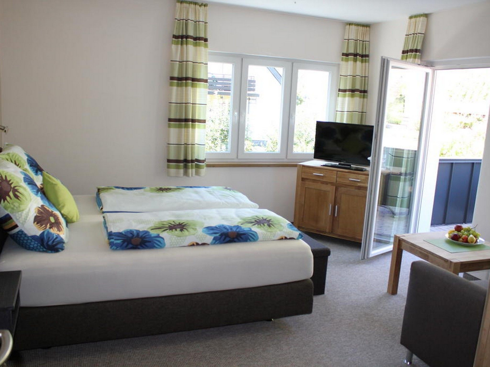 A bedroom with a bed, a television, a wooden cabinet, and a table with fruit.
