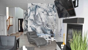 Un saló modern amb un sofà gris, una taula de centre, una llar de foc i un quadre abstracte gran a la paret.