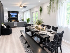 Un espace repas moderne avec une longue table dressée pour six personnes, entourée de chaises noires ornées de motifs blancs.