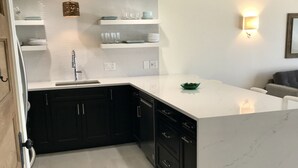 A modern kitchen with black cabinets, a white countertop, and a marble backsplash. - Beachfront Condo, 1 King Bedroom + Bunk, 2 baths, sleeps 5 (Destin)