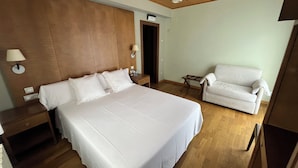 A hotel room with a large bed, a white armchair, a wooden ceiling, and a small table. - Hotel Vall Fosca (La Torre de Cabdella)