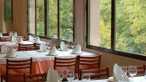 A dining area with tables set for service, large windows with a view of trees, and a painting on the wall. - Hotel Vall Fosca (La Torre de Cabdella)