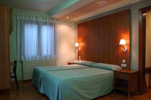 A hotel room with two beds, a wooden headboard, two bedside lamps, a radiator, and a window with curtains. - Hotel Vall Fosca (La Torre de Cabdella)