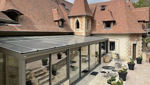 A traditional building with a glass conservatory, stone steps, and outdoor seating. - Le Prieure des Fontaines (Les Preaux)