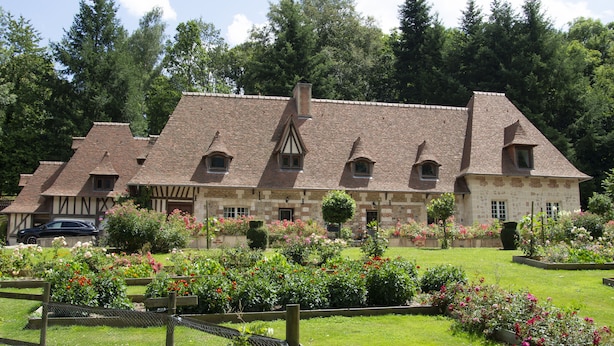 A traditional stone building with a sloped roof, multiple windows, and a well-maintained garden with various plants and flowers. - Le Prieure des Fontaines (Les Preaux)