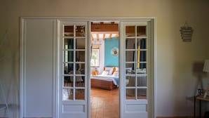 A room with a bed, a chair, and a table. There is a door leading to another room. - Le Prieure des Fontaines (Les Preaux)