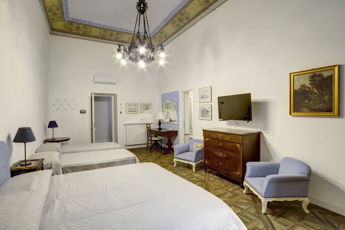 A hotel room with two beds, a desk, a dresser, a TV, and a painting on the wall.
