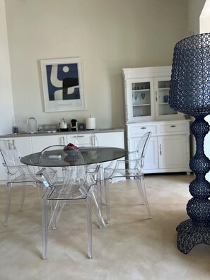 A modern kitchen with a glass dining table, clear chairs, and a decorative blue lamp.