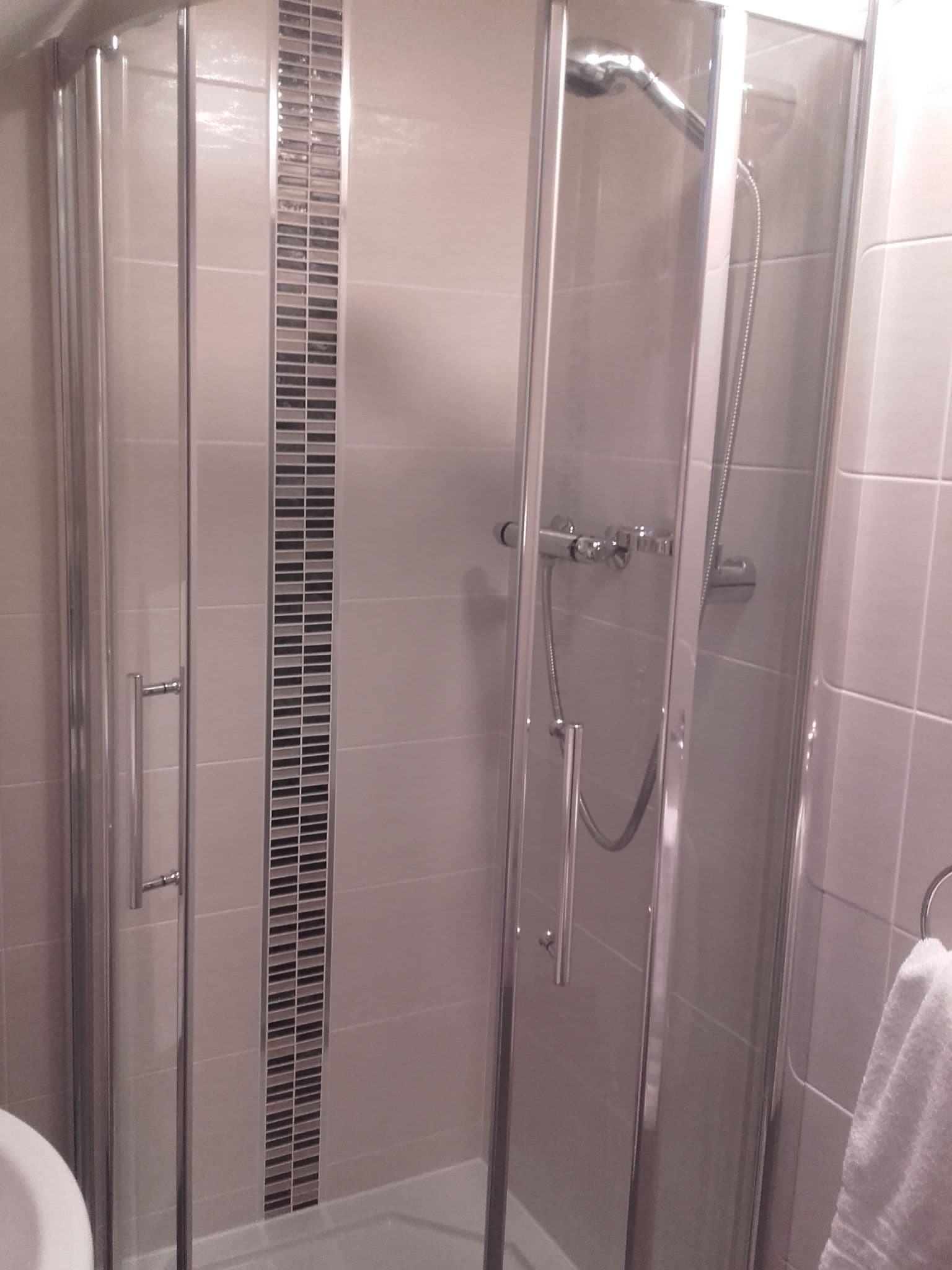 A glass-enclosed shower with a handheld showerhead and a wall-mounted faucet.