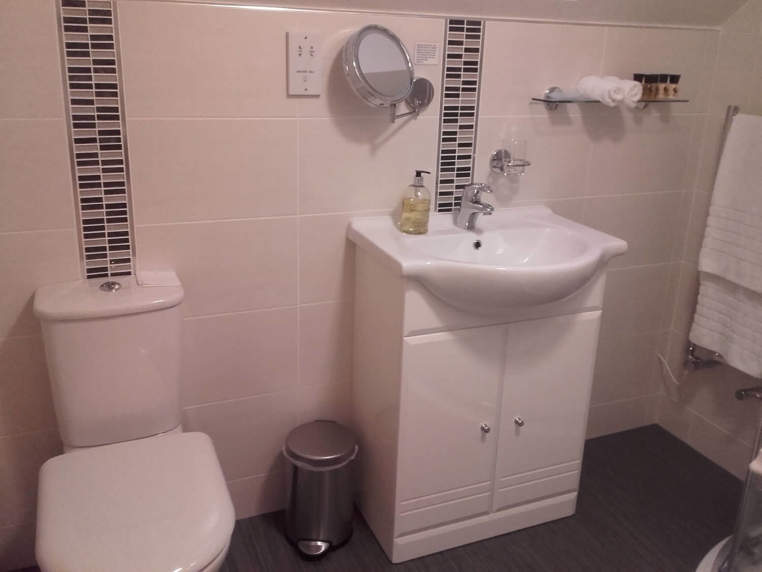 A bathroom with a toilet, a sink with a mirror, a trash bin, and a towel rack.