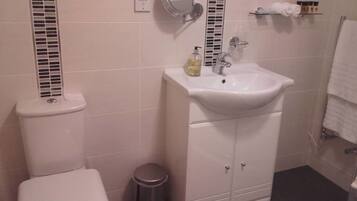 A bathroom with a toilet, a sink with a mirror, a trash bin, and a towel rack.