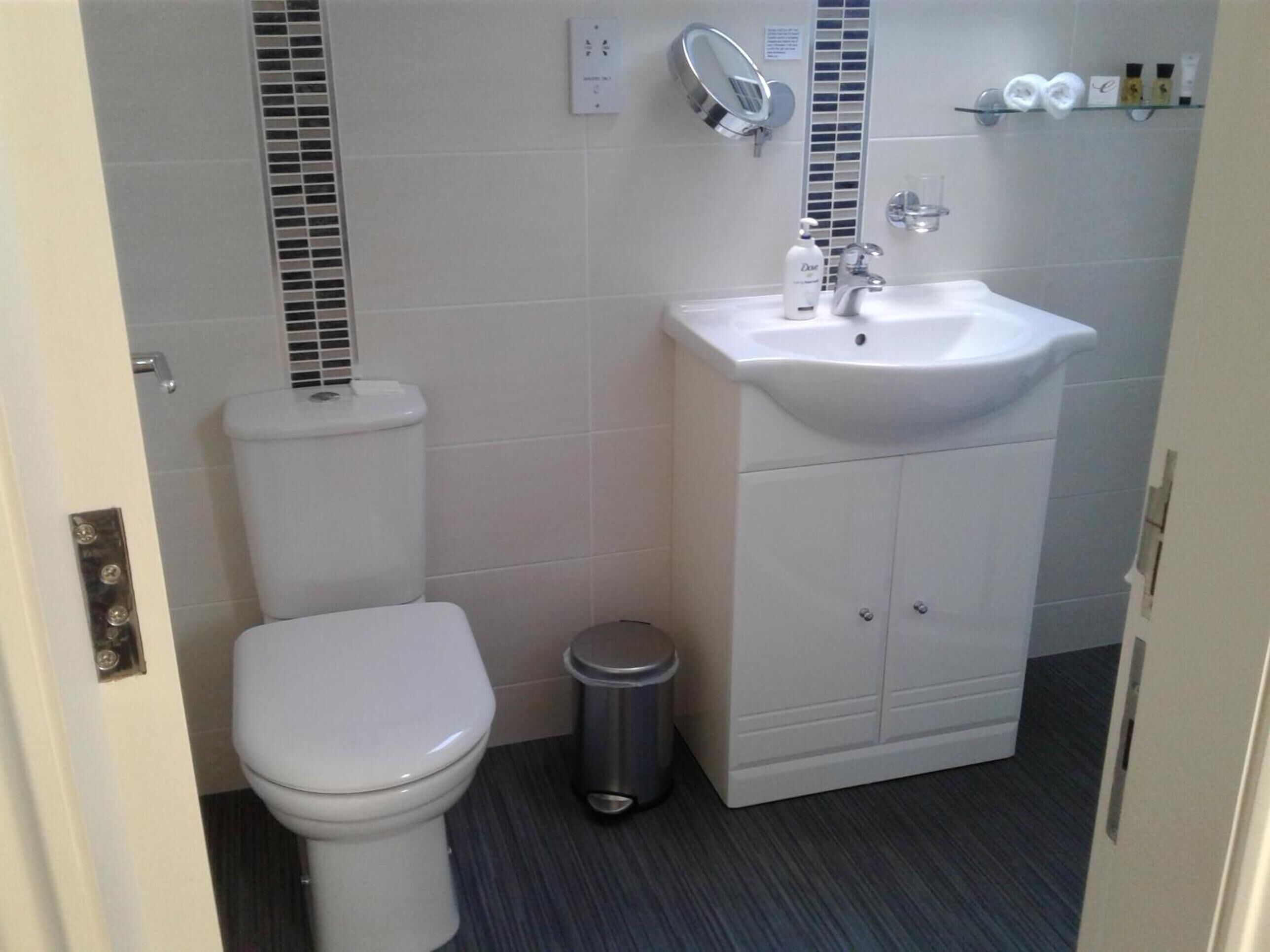 A modern bathroom with a white toilet, a sink with a mirror, and toiletries on a shelf.