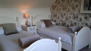 Une chambre avec deux lits, une table de chevet avec une lampe et un papier peint à motifs floraux.