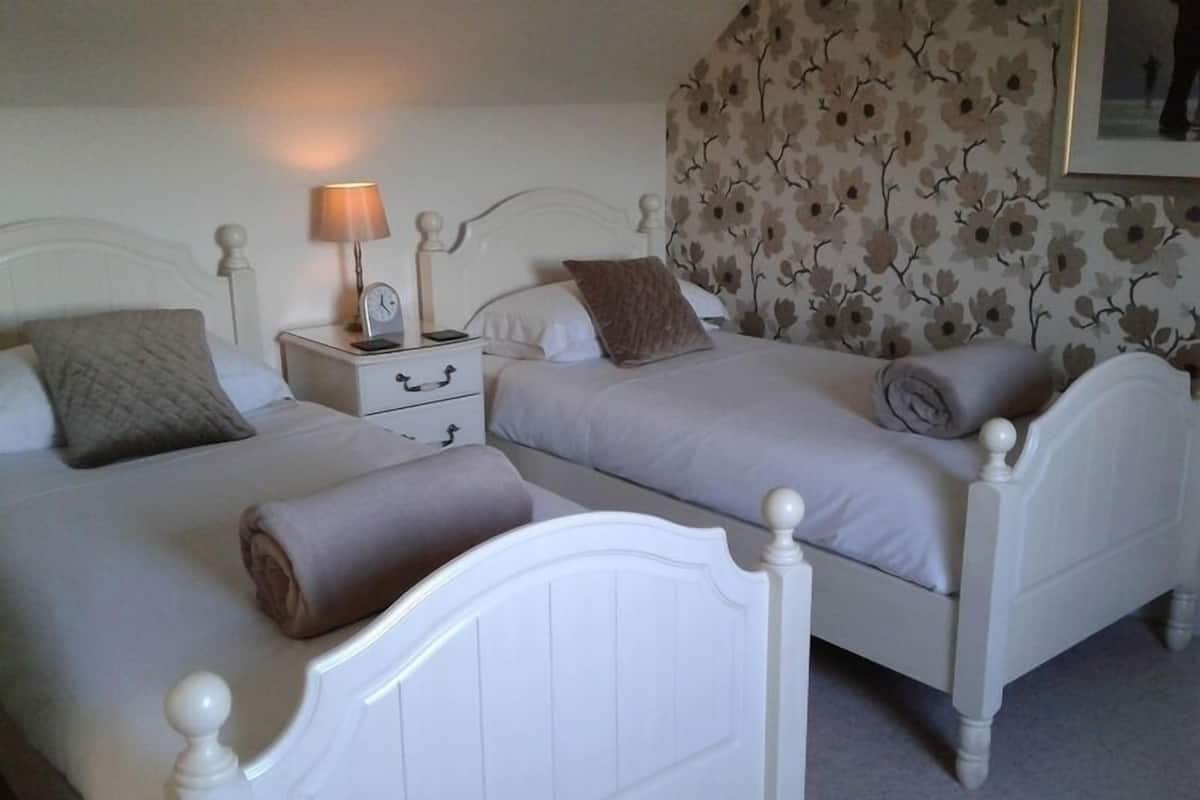 Een slaapkamer met twee bedden, een nachtkastje met een lamp en bloemenbehang.