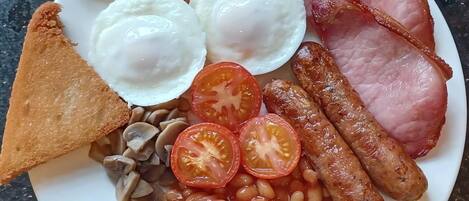 A plate of breakfast food including eggs, bacon, sausages, toast, beans, and tomatoes.