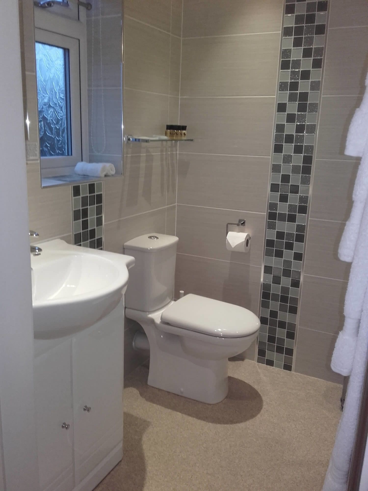 Et badeværelse med en hvid vask, toilet og bruseområde.