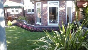 Une maison en briques avec une pelouse bien entretenue, un espace patio et un jardinière suspendue.