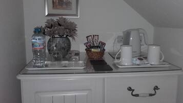 A kitchen counter with a coffee maker, two mugs, a basket of snacks, and a water bottle.