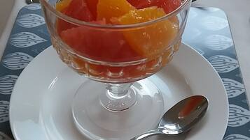 Un dessert aux fruits servi dans un bol en verre, posé sur une assiette blanche avec une cuillère à côté, le tout placé sur une table recouverte d’une nappe à motifs bleus.