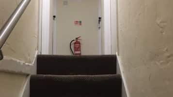 A staircase with carpeted steps leading to a door with a fire extinguisher mounted on the wall.