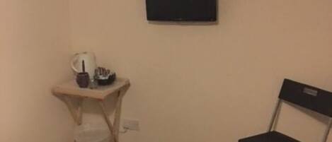 A small room with a bed, a desk, a chair, and a television on the wall.