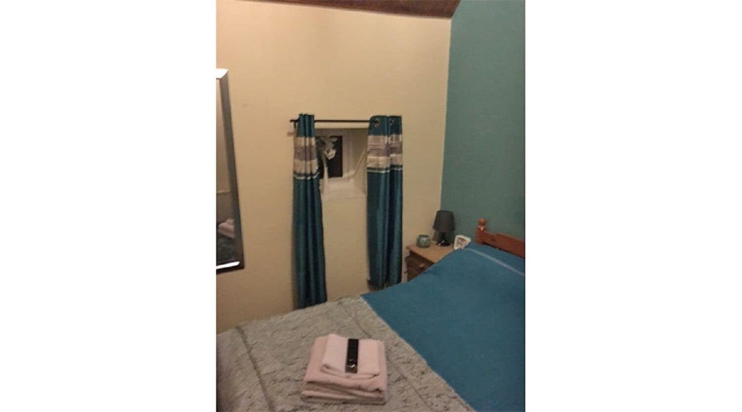 A bedroom with a bed, a nightstand, a lamp, and a window with curtains.