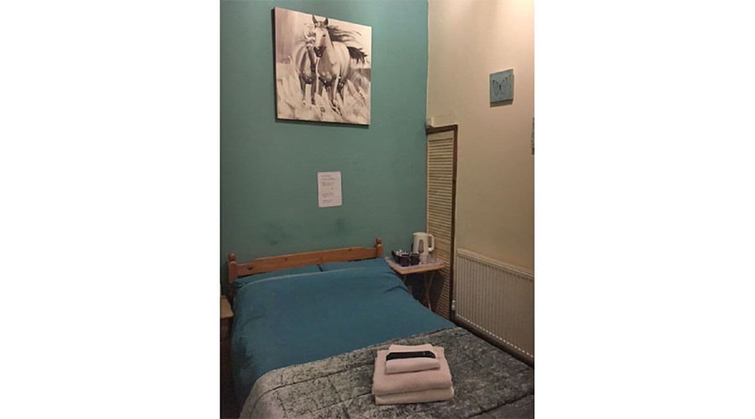 Un dormitorio con cama, mesita de noche, un reloj de pared y un cuadro de un caballo.