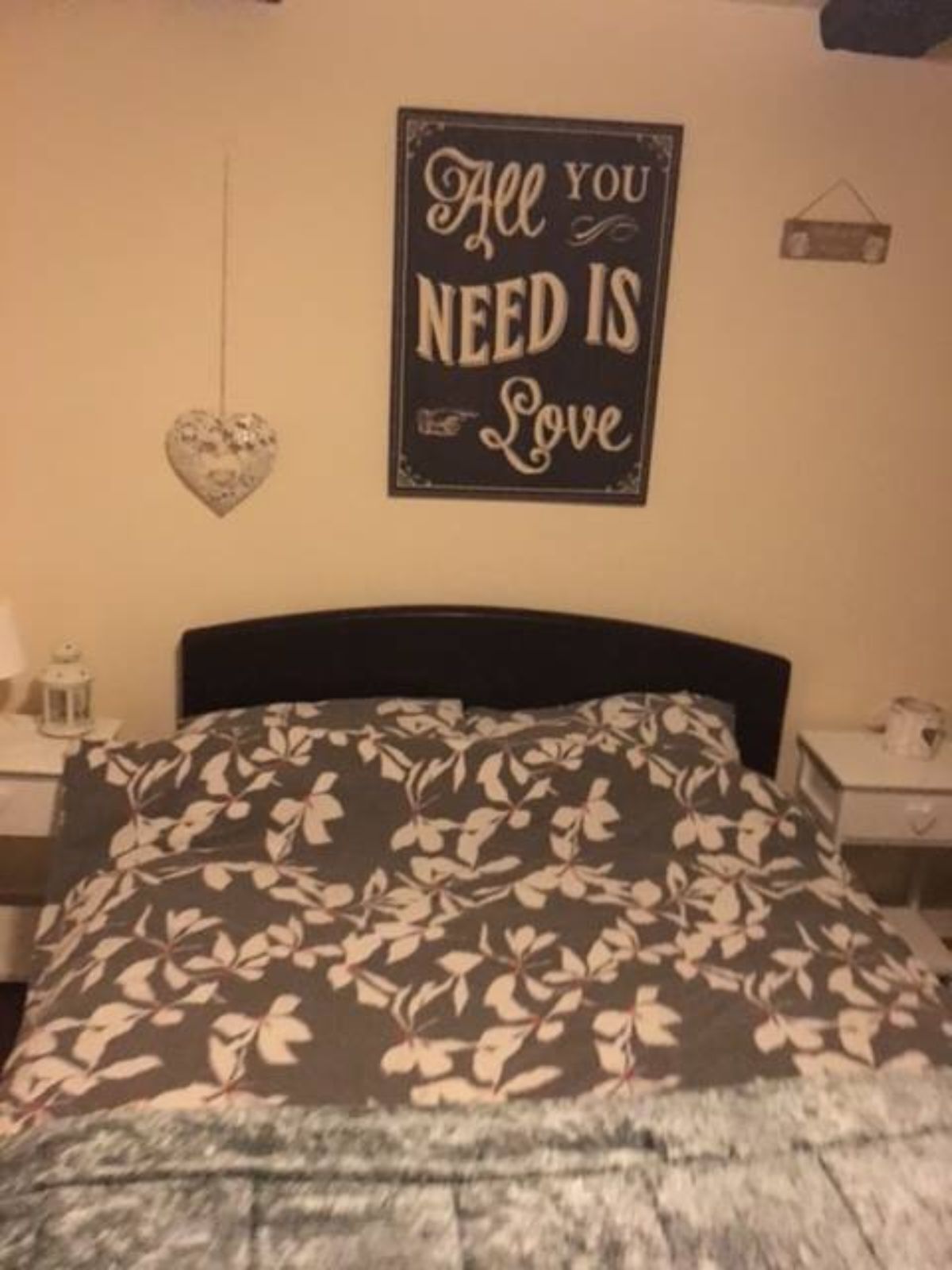 Un dormitorio con cama, mesita de noche, reloj de pared y un letrero decorativo que dice 'All You Need Is Love'.