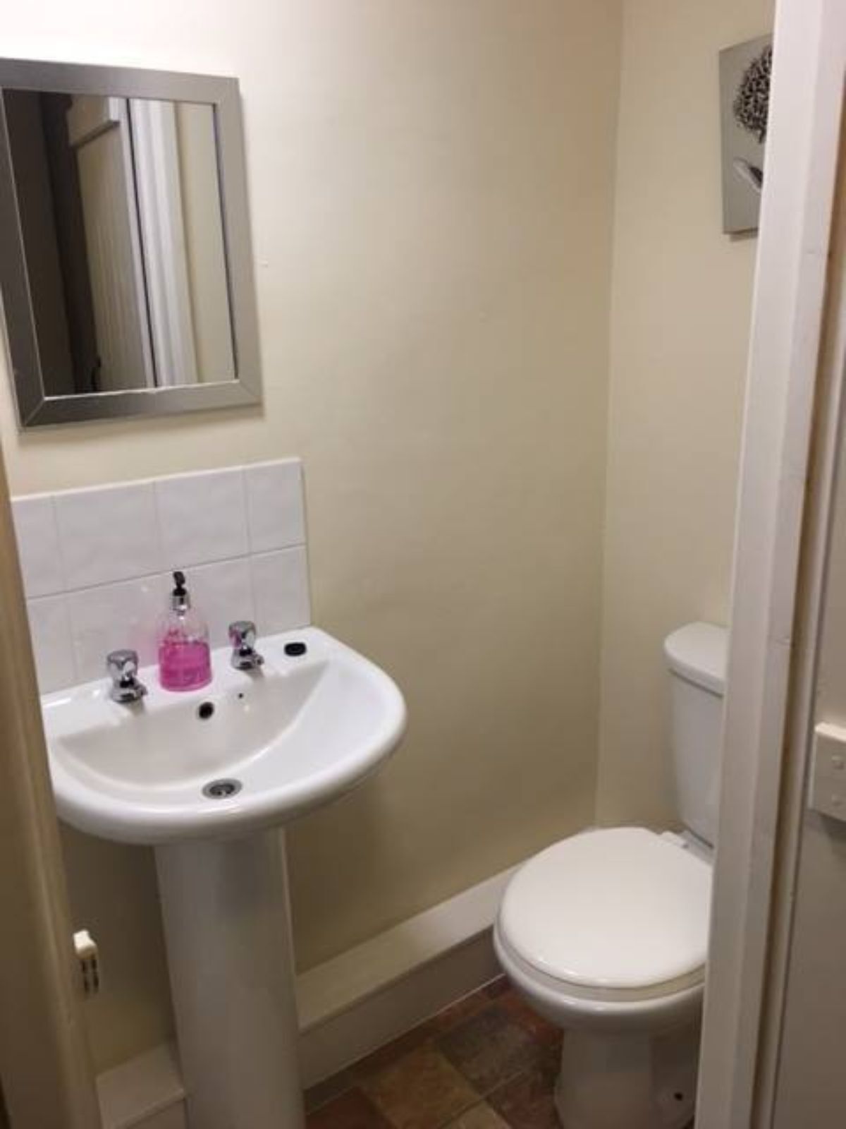 Un baño con lavamanos pedestal, inodoro y espejo en la pared.
