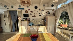 A kitchen with a dining area, featuring a table with a colorful rug, a hanging light fixture, and various decorative items on the walls.