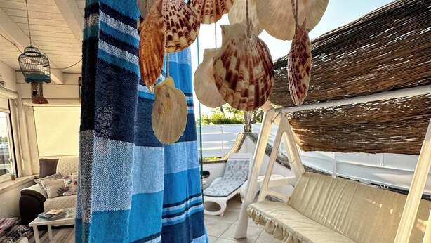 A room with a blue striped curtain, a white bench, and hanging seashells.